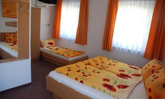 A cozy bedroom with two beds and bright orange decorations. The curtains let in a lot of daylight.