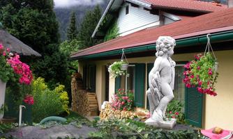 An idyllic house surrounded by colorful flowers and green plants. In the foreground stands a statue that complements the overall picture.