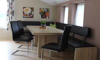 A modern dining area with a wood-colored table and black chairs. On the wall, there are two colorful pictures of food.