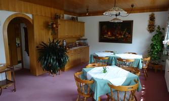 A cozy dining room with wooden paneling and bright tables. Green plants and a decorative mural create an inviting atmosphere.