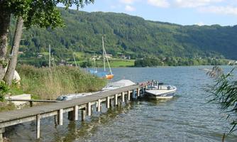 A picturesque pier by the water with a boat. In the background, green hills and more boats can be seen.