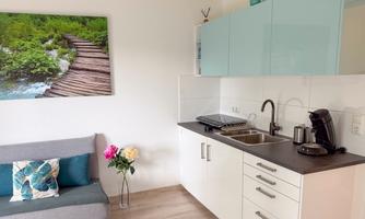 A modern kitchen with bright furniture and a cozy sofa. A picture of a green landscape hangs on the wall.