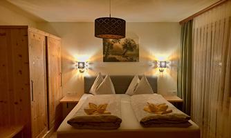 A cozy bedroom with a double bed and wooden furniture. Soft lighting and a picture on the wall create a relaxed atmosphere.