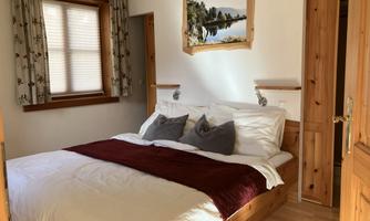 A cozy bedroom with a large bed and soft pillows. There are wooden paneling and a window with curtains.