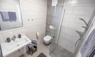 A modern bathroom with a glass shower and sanitary facilities. The walls are light tiled, and towels are neatly arranged.