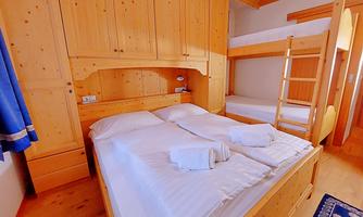 A cozy room with wooden furniture and a double bed. In the background, there is a bunk bed and there are fresh towels.