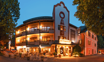 A charming hotel with a cozy restaurant on the ground floor. The façade of the building is styled in a traditional manner and is surrounded by trees.