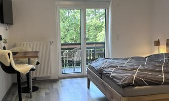 A modern room with a large bed and a table.  
Large windows offer a view of greenery.