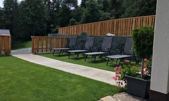 A green meadow with loungers and a wooden fence in the background. Colorful flowers in pots are located at the edge of the walkway.