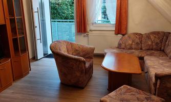 A cozy living area with a sofa set and a wooden table. The room has large windows that let in plenty of light.