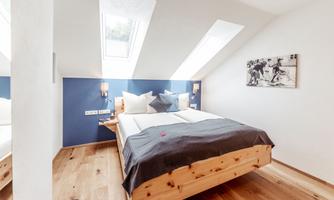 A modern bedroom with a double bed and plenty of natural light. The walls are painted in a calm blue and the floor is wooden.