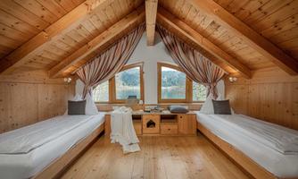 A cozy bedroom with a wooden ceiling and two single beds. Large windows offer a view of nature.