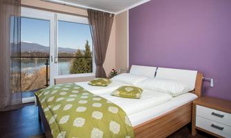 A cozy bedroom with a large window overlooking a lake. The walls are painted in soft colors, and the duvet has a romantic pattern.