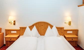 A cozy room with a double bed and two nightstands. The walls are light, and there are ambient wall lamps.