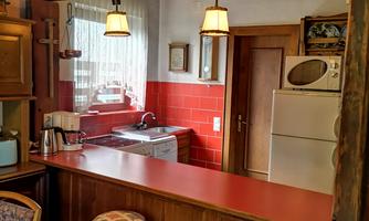 A warm and cozy kitchen with red tiles and wooden shelves. The room has a small countertop with chairs and modern kitchen appliances.