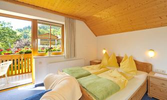 An inviting bedroom with a wooden ceiling and a large window. The two beds are decorated with yellow and green pillows, and the room has a view of the outdoor area.
