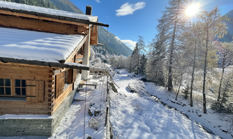 A cozy wooden house in a winter landscape. The surroundings are covered with snow and the sun is shining clearly in the blue sky.