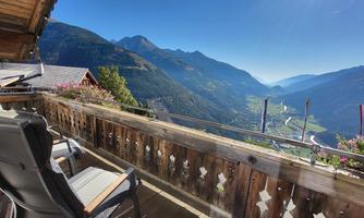 A beautiful balcony with a view of a valley and mountains. The sun is shining and the landscape is green and inviting.