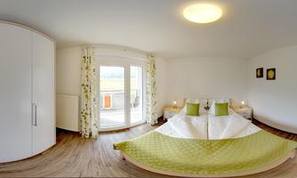 A modern bedroom with a large bed and pleasant decor. Large windows provide a view of the outdoors and ensure plenty of daylight.