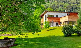 A modern house amidst a green landscape. The garden is surrounded by trees and offers a quiet seating area.
