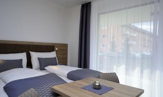 A modern bedroom with two beds, a cozy decor, and large windows. The room is bright and inviting, perfect for relaxation.