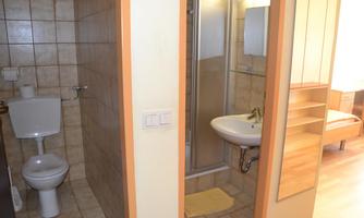 A small bathroom with a shower, a sink, and a toilet. The walls are tiled and the floor is light.