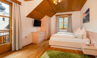 A cozy bedroom with two beds and a wooden ceiling. Large windows let in plenty of light and offer a view outside.