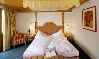 A cozy hotel room with a large bed and comfortable chairs. The walls are painted in light colors and decorated with artworks.