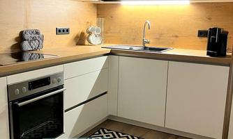 A modern kitchen with wooden and white furniture. The room is well-lit and features an elegant rug with a geometric pattern.
