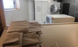 A modern bathroom with bright tiles and a large window. Towels hang on the wall and a sink is visible.