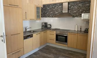 A modern kitchen with wooden cabinets and an elegant stone backsplash. The appliances are stylishly integrated and it offers ample counter space.