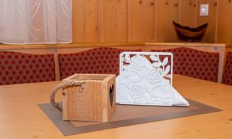 A decorative wooden box and a white table stand with a floral pattern are on a table. The background is made of wood and shows a cozy atmosphere.