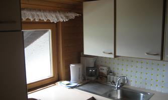 A small, bright kitchen with a window and wooden ceiling. The wall has a yellow polka dot pattern and kitchen appliances are visible.