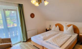 A cozy bedroom with two beds and white bedding. There is a window overlooking the balcony and a pleasant seating area.