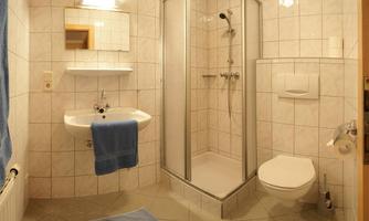 A modern bathroom with a shower, a sink, and a toilet. The walls are tiled and there is a large mirror.