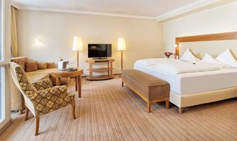 A modern hotel room with a double bed, a television, and a cozy seating area. The colors are bright and friendly, with plenty of natural light.