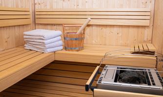 A cozy sauna with wooden benches and soft towels. In the background, a wooden container and a sauna stone stove can be seen.