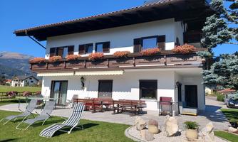 A beautiful house with a large garden and terrace. Outside, there are sun loungers and blooming plants at the windows.