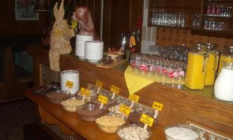 A buffet with various breakfast items, including cereal, yogurt, and drinks. In the background, glasses and a decorative figure can be seen.