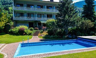 An elegant building with several balconies, surrounded by green landscapes. In front of the building, there is an inviting pool in a well-maintained garden.