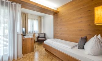A simple and modern single room with wooden details. There is a bed, an armchair, and a small table.