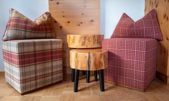 Two cozy upholstered stools with a checkered cover and a round wooden table stand in a corner. The floor is made of wood and gives the room a warm atmosphere.