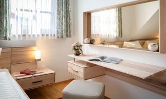 A bright room with a wooden desk and a mirror. The windows are decorated with curtains and there are decorative elements on the table.