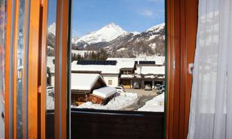 A view from a window of snow-covered mountains and a quiet village. The sun is shining and the sky is clear.