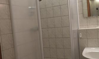 A modern bathroom with a glass shower. The walls are tiled and a sink is visible.
