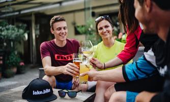 A group of friends clinks drinks together. They enjoy a relaxed atmosphere outdoors.