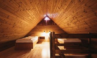 A cozy wooden attic room with two single beds and a bunk bed. The walls are also made of wood, creating a warm atmosphere.