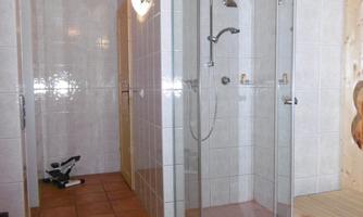 A modern bathroom with a large shower and tiled floor. The walls are tiled in light colors and there is wood paneling on the ceiling.