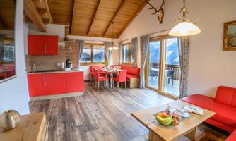 A bright and modern apartment with an open kitchen and dining area. The red furniture and wooden walls create a cozy atmosphere.