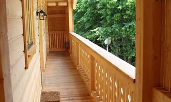 A cozy wooden balcony with a clear view of green trees. The walls and floor are made of light wood.